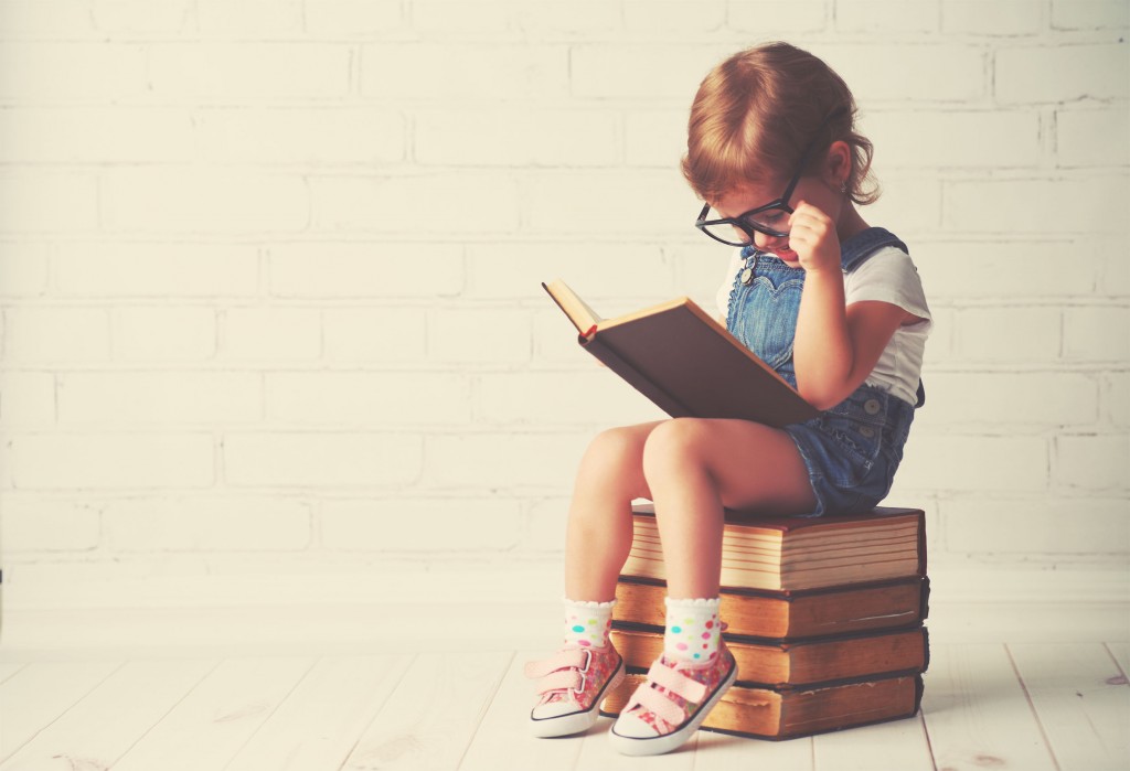 50959358 - happy child little girl with glasses reading a books