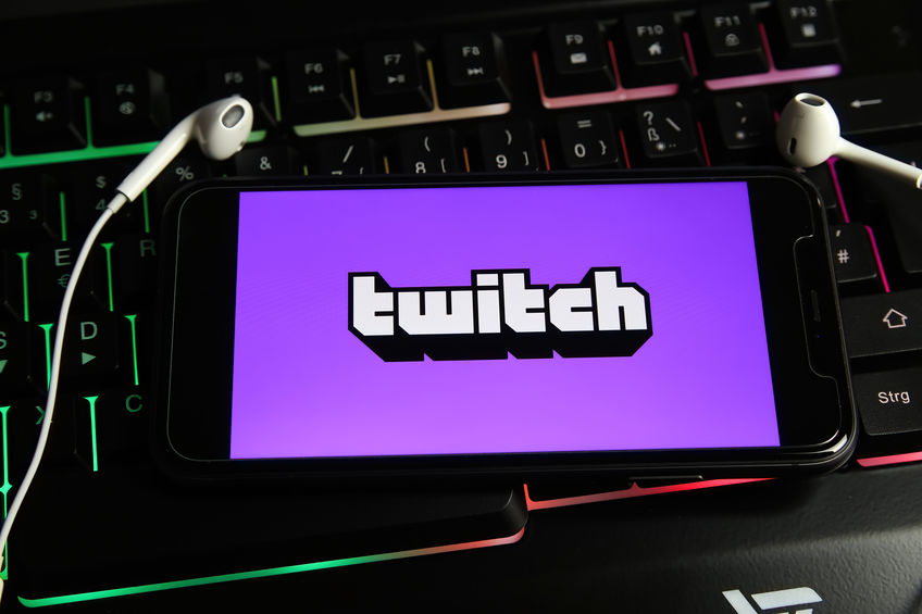 Viersen, Germany - February 9. 2021: Closeup of smartphone screen with logo lettering of video live streaming platform twitch on computer keyboard